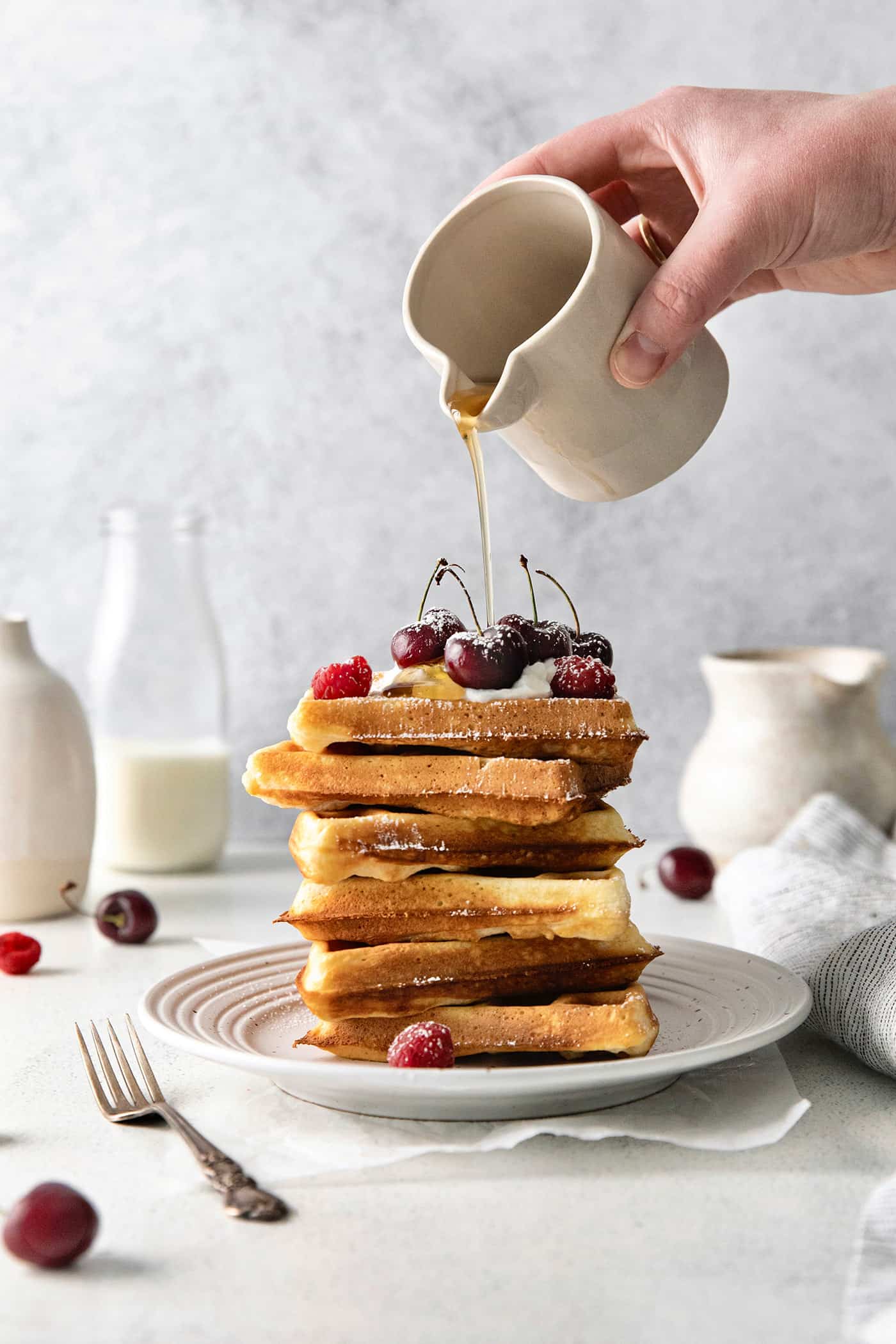 A hand pouring syrup over a stack of homemade waffles