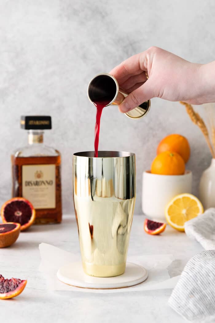 pouring blood orange juice into a cocktail shaker