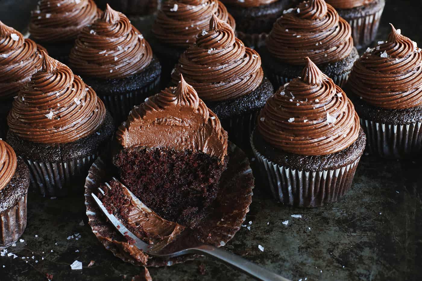 Chocolate cupcakes topped with chocolate buttercream, one cut in half