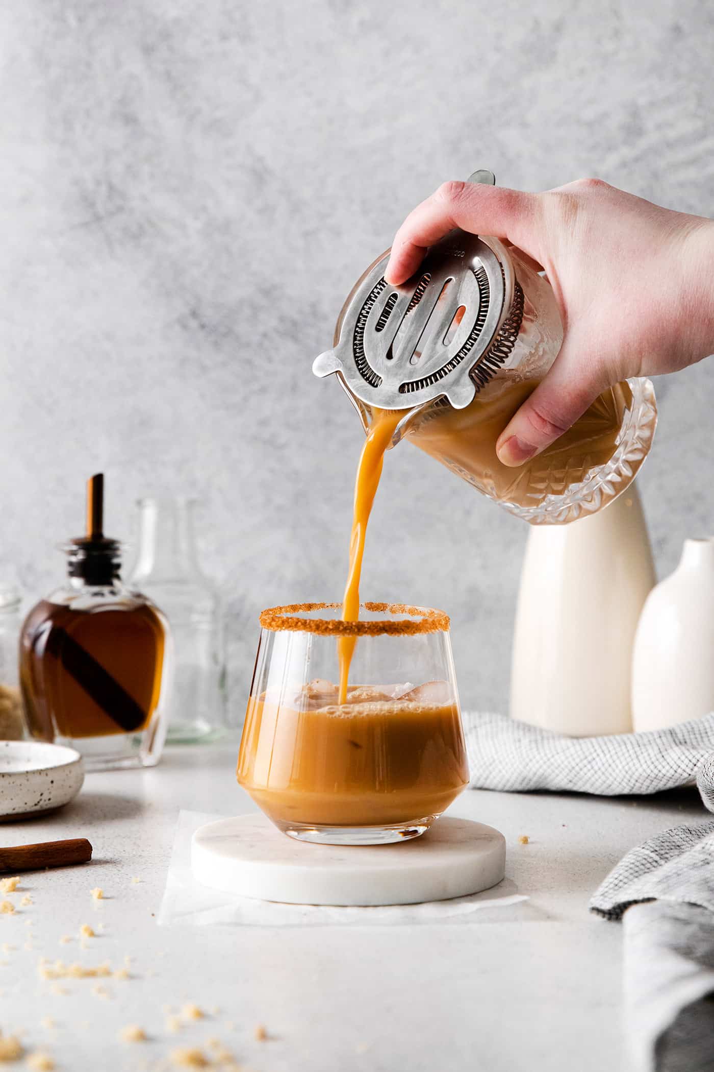 pouring finished eggnog white Russian cocktail into a glass with a cinnamon sugar rim