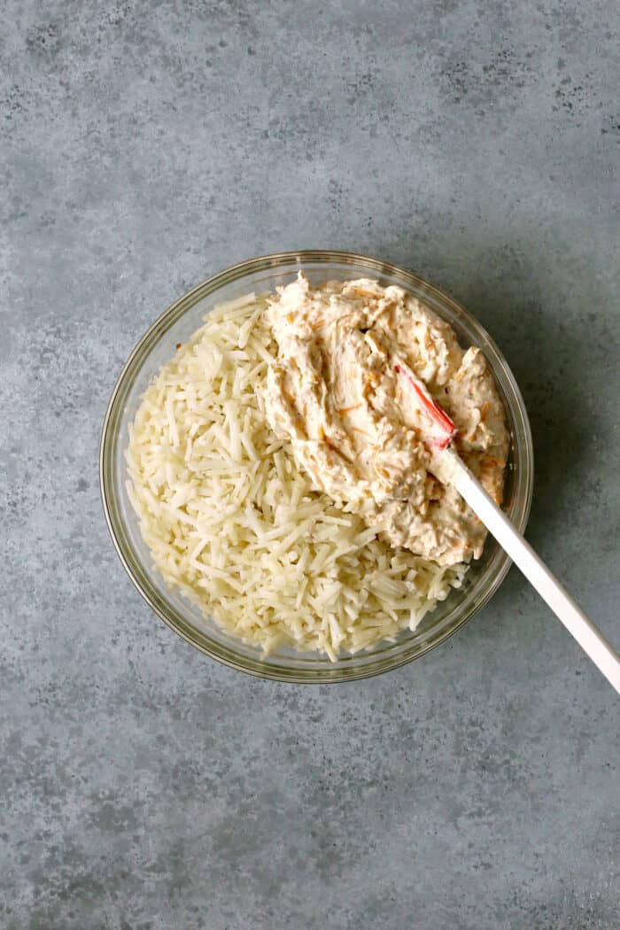 Hashbrowns and a cheese mixture being mixture together in a white bowl