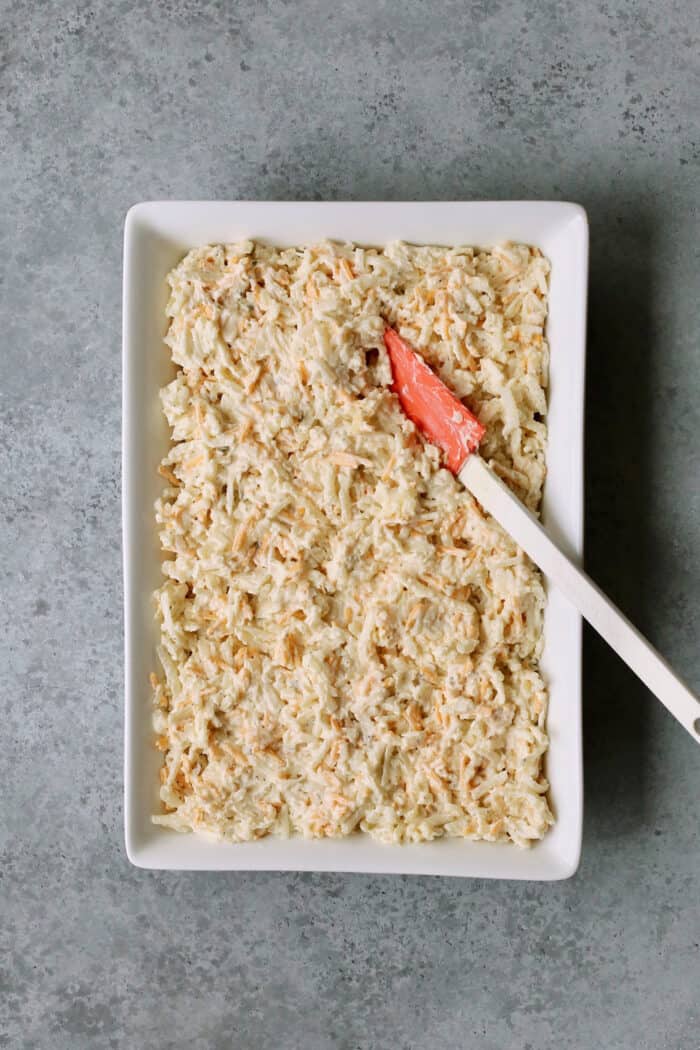 Hashbrown casserole mixture being spread in a white baking dish