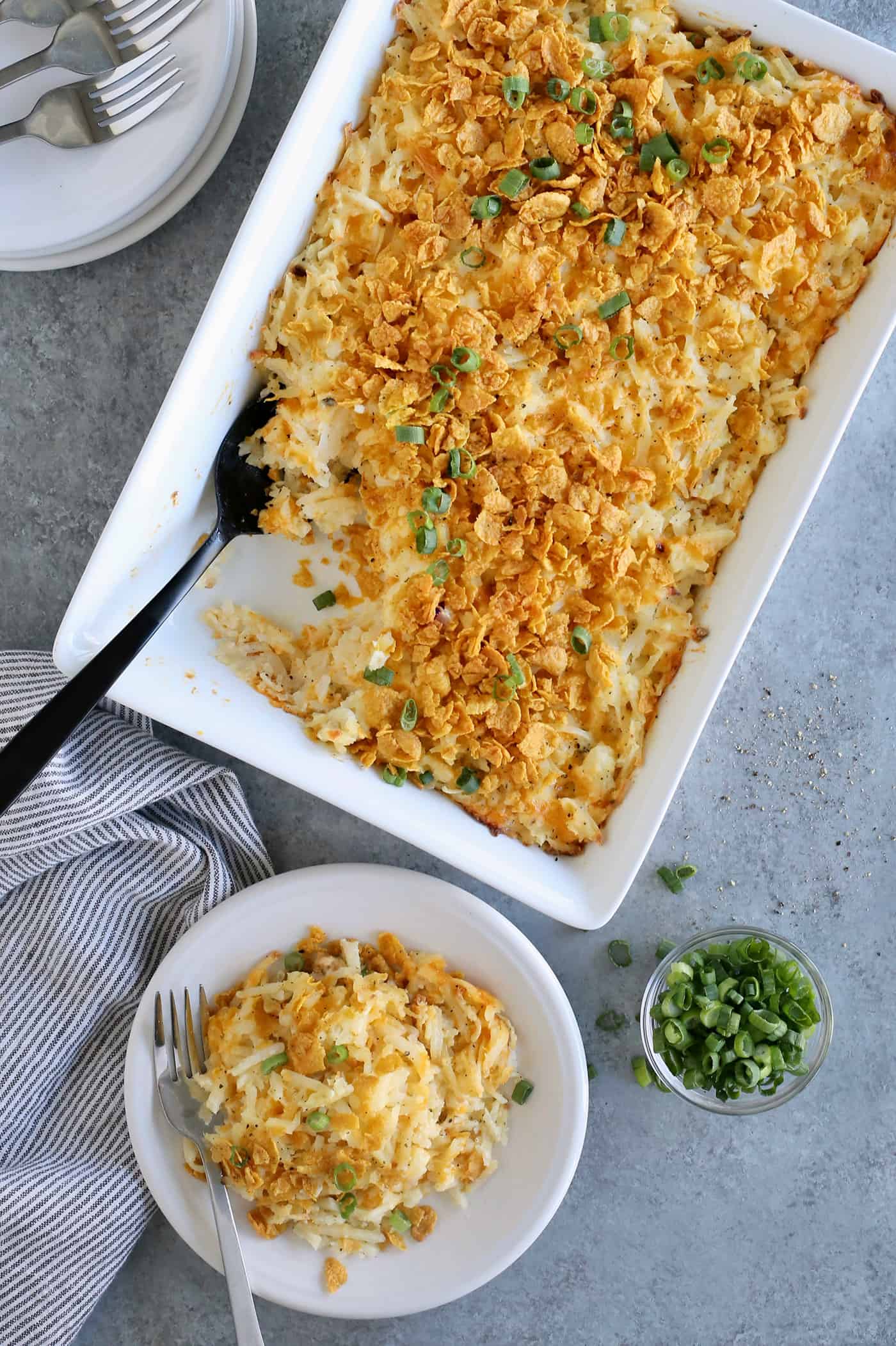 an individual serving of hashbrown casserole on a white plate, next to the baking dish