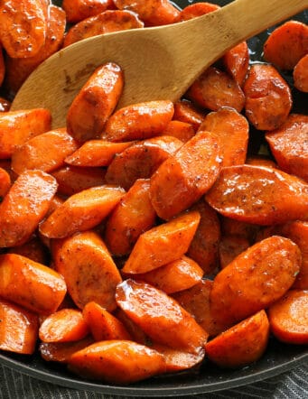 A wooden spoon stirring cinnamon honey carrots