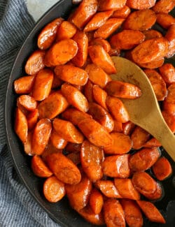 Overhead view of a wooden spoon stirring cinnamon honey carrots