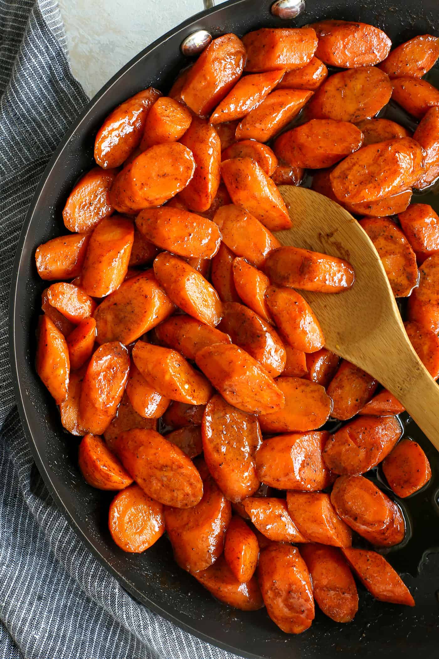 Overhead view of a wooden spoon stirring honey glazed carrots