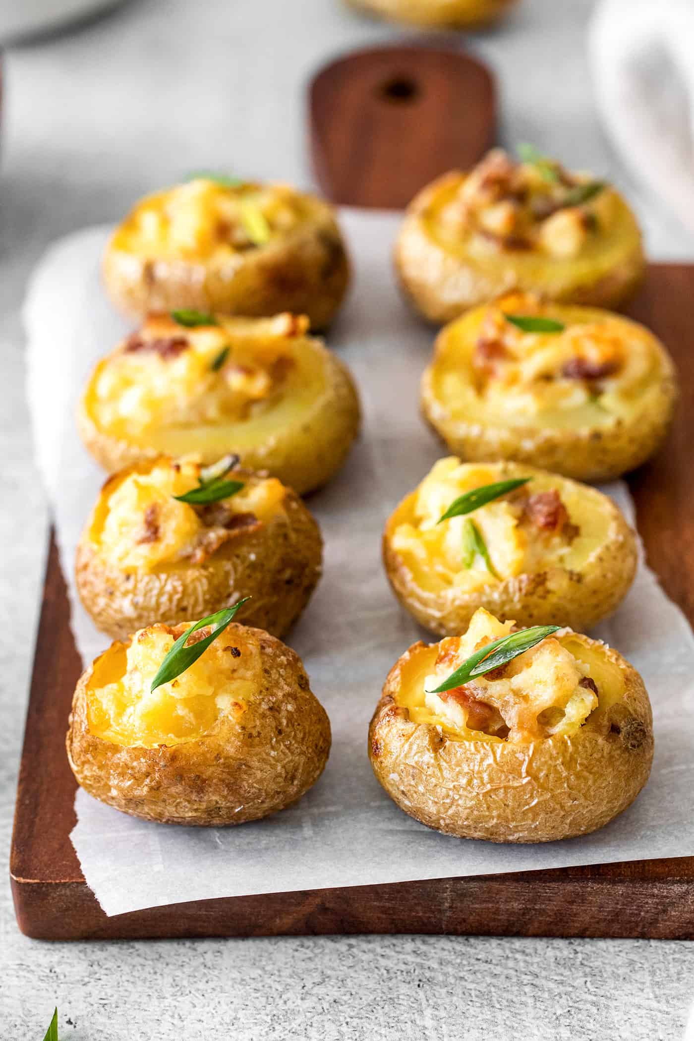 Angled view of loaded baked potato bites on parchment paper on a cutting board