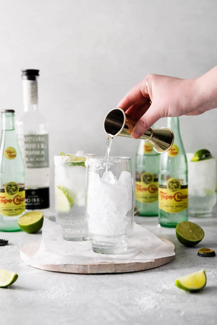 A hand pouring tequila into a glass with ice