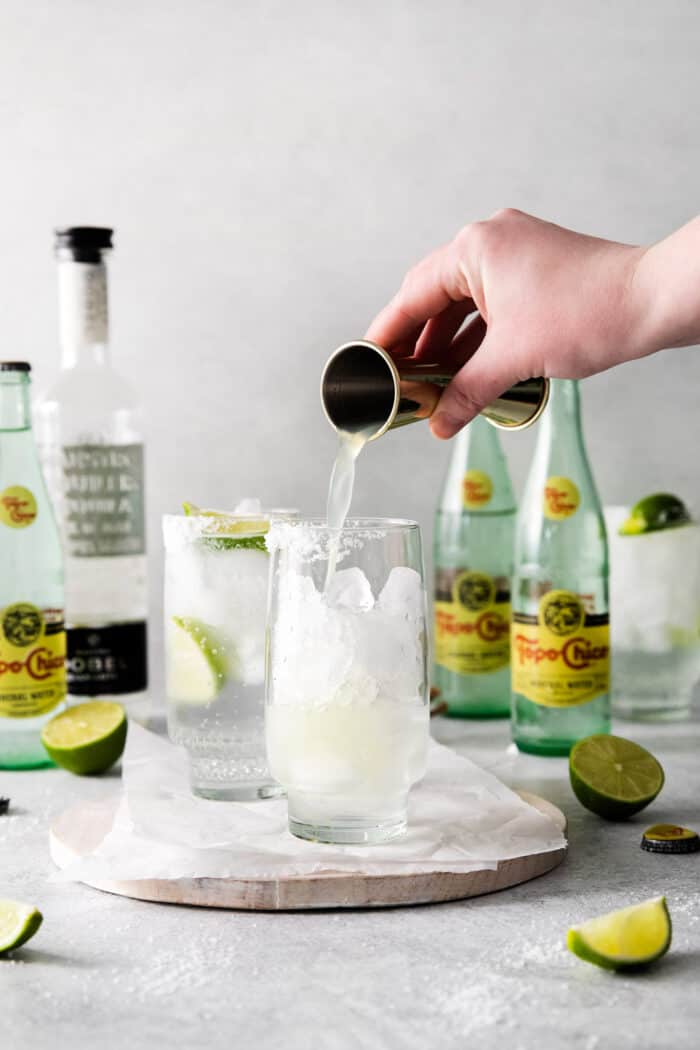 A hand pouring lime juice into a glass with ice