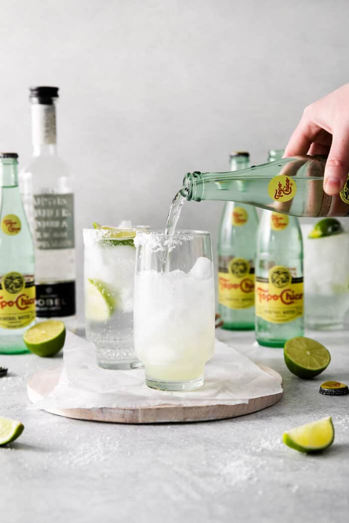 A hand pouring Topo Chico into a glass with ice