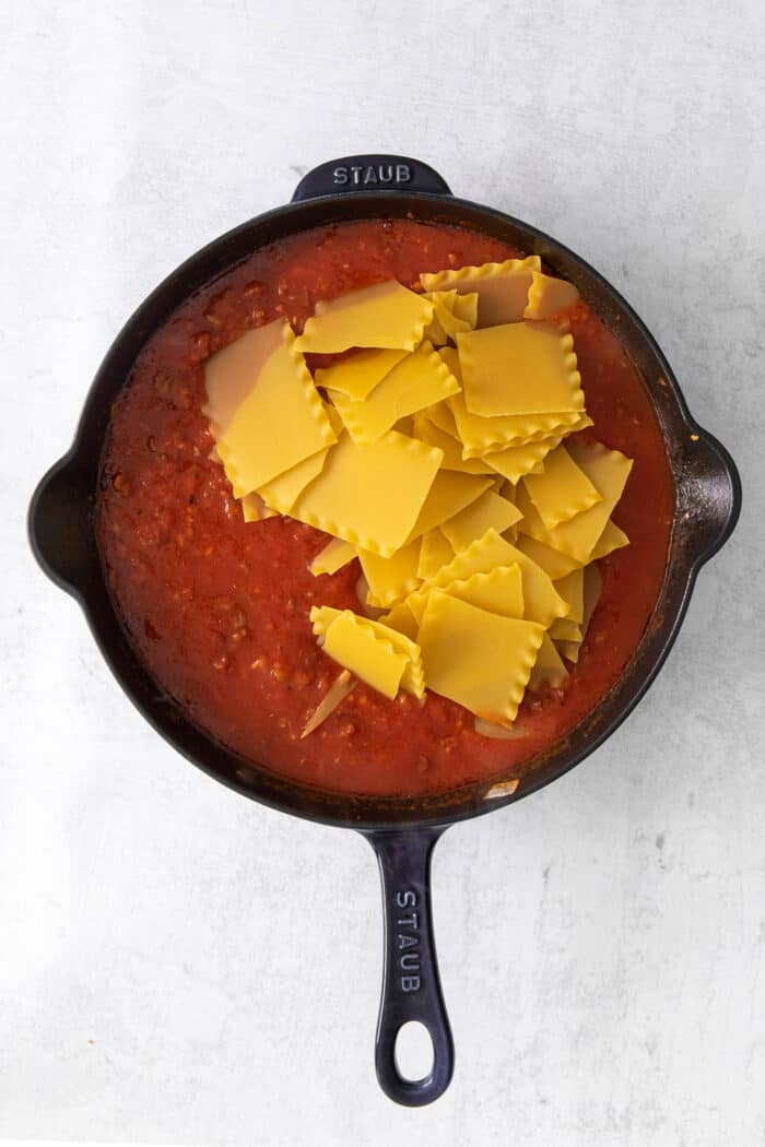 Broken lasagna noodles and marinara sauce in a cast iron skillet