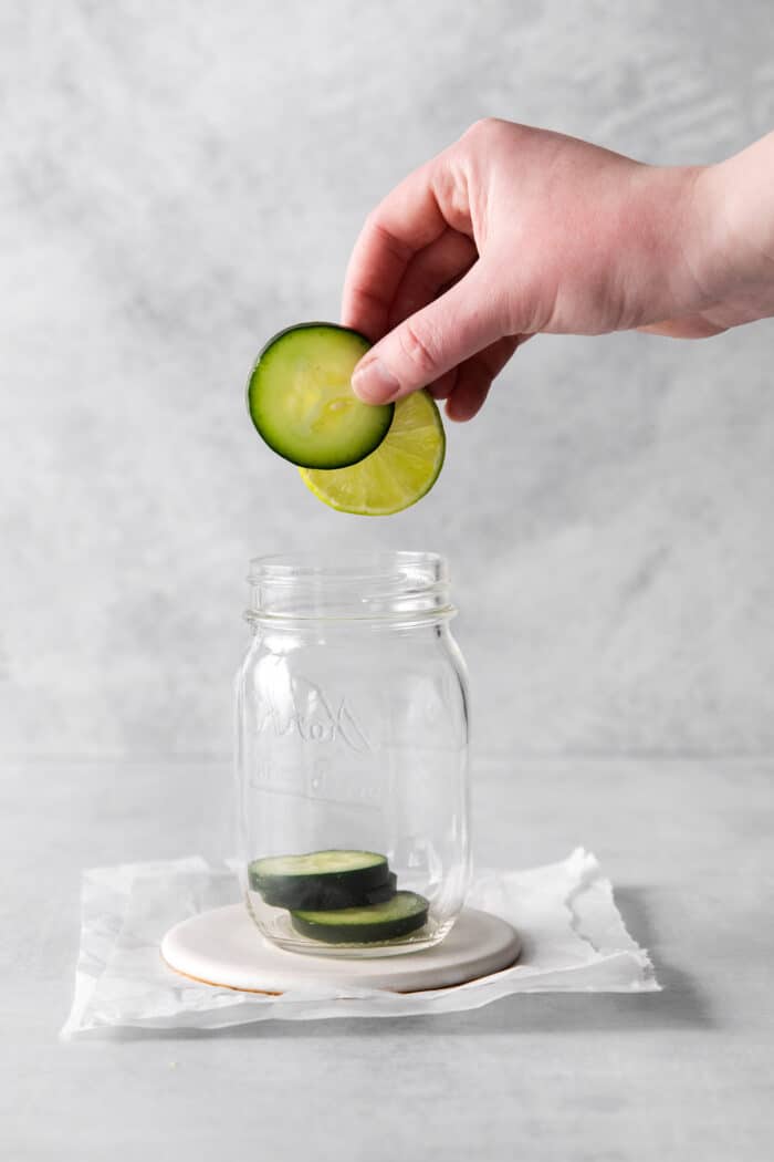 Slices of cucumber being added to a mason jar