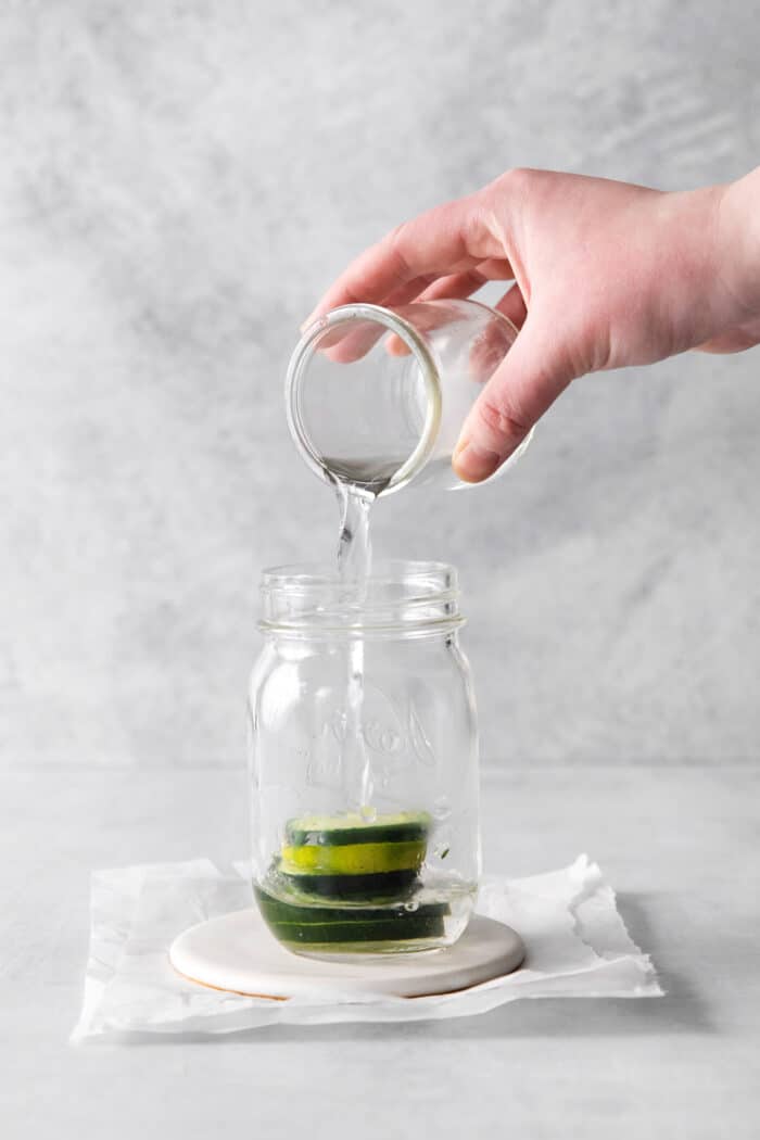 Tequila being added to a glass jar with cucumber slices