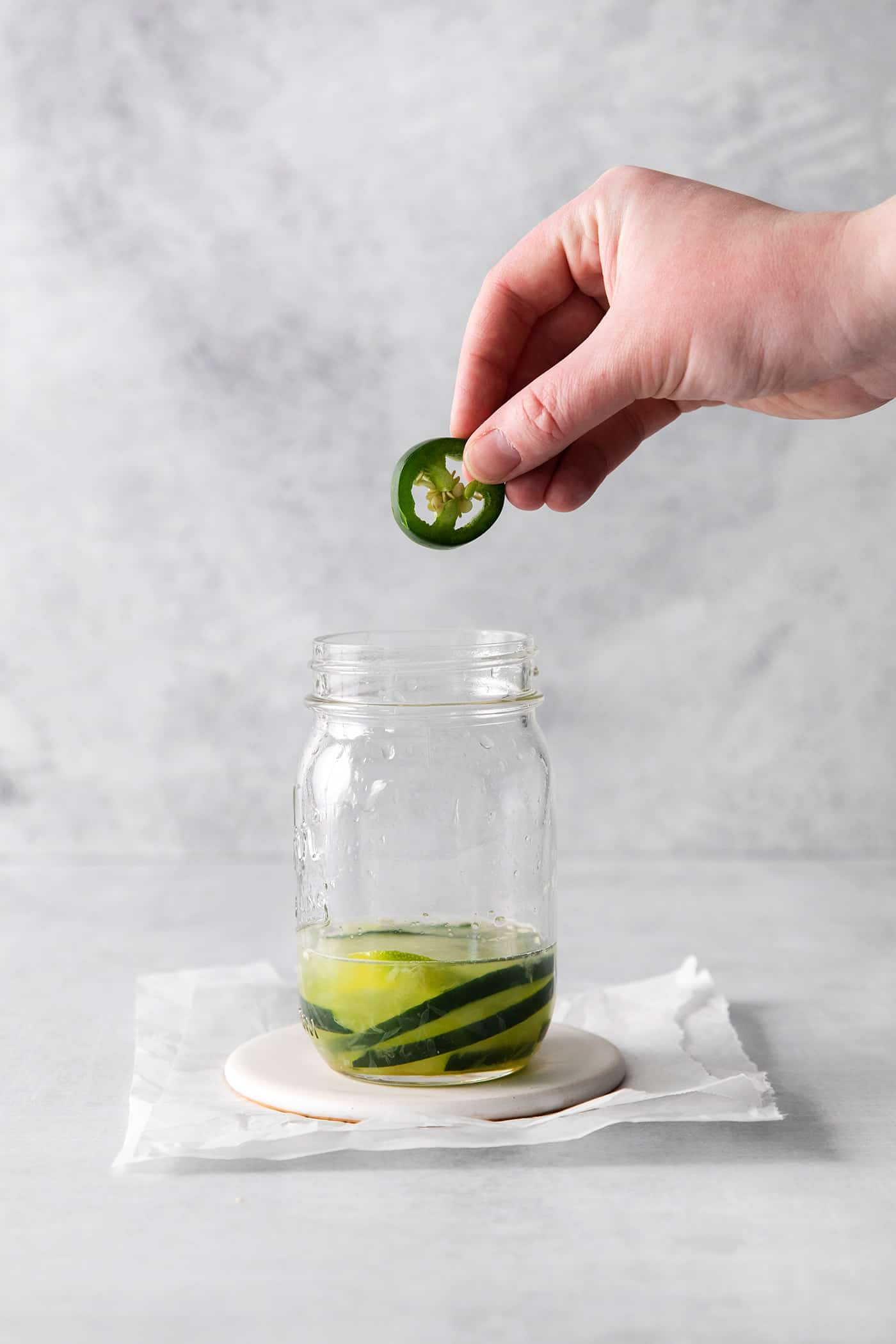A jalapeno being dropped into a glass with cucumber slices