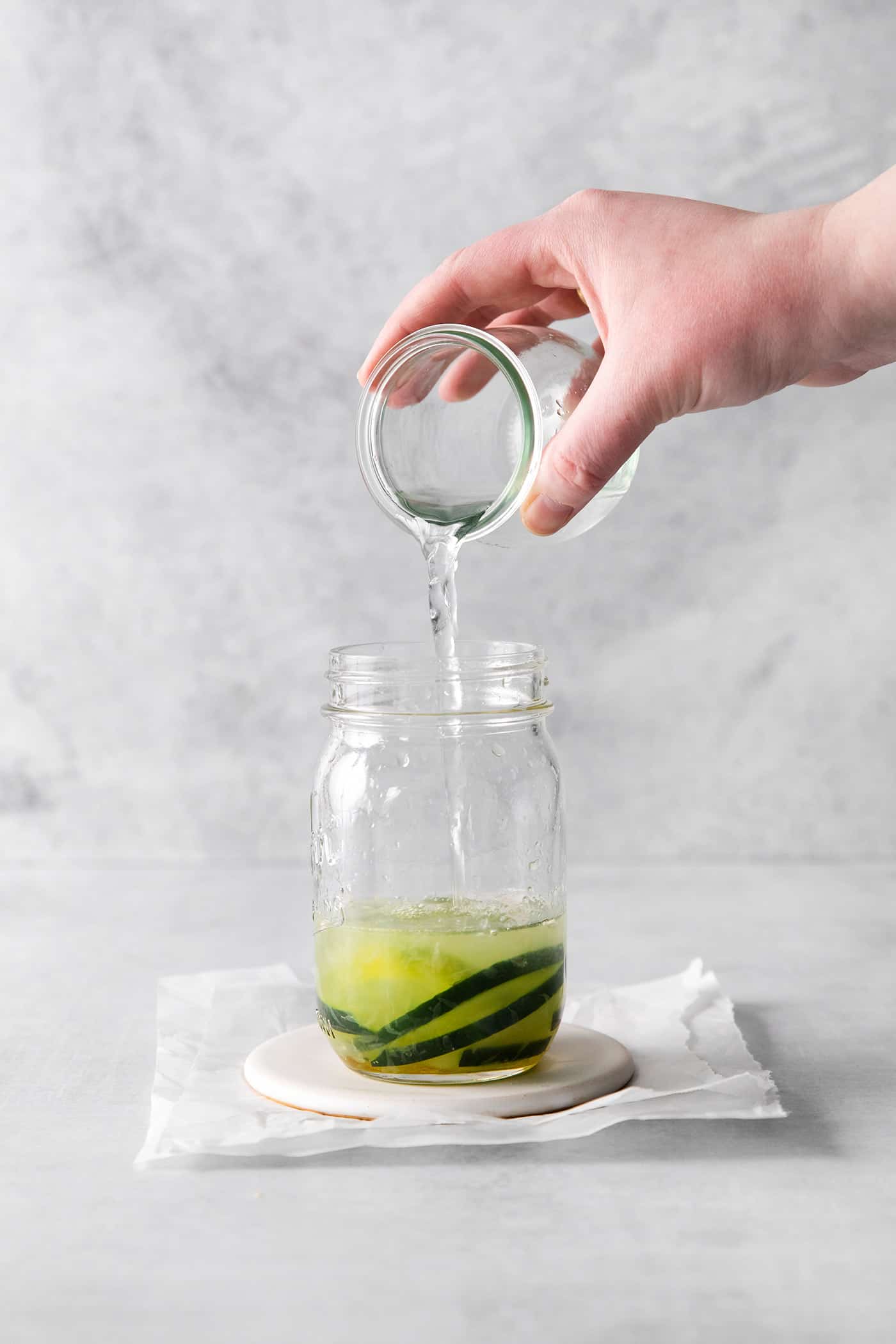 Tequila being added to a glass with cucumber slices