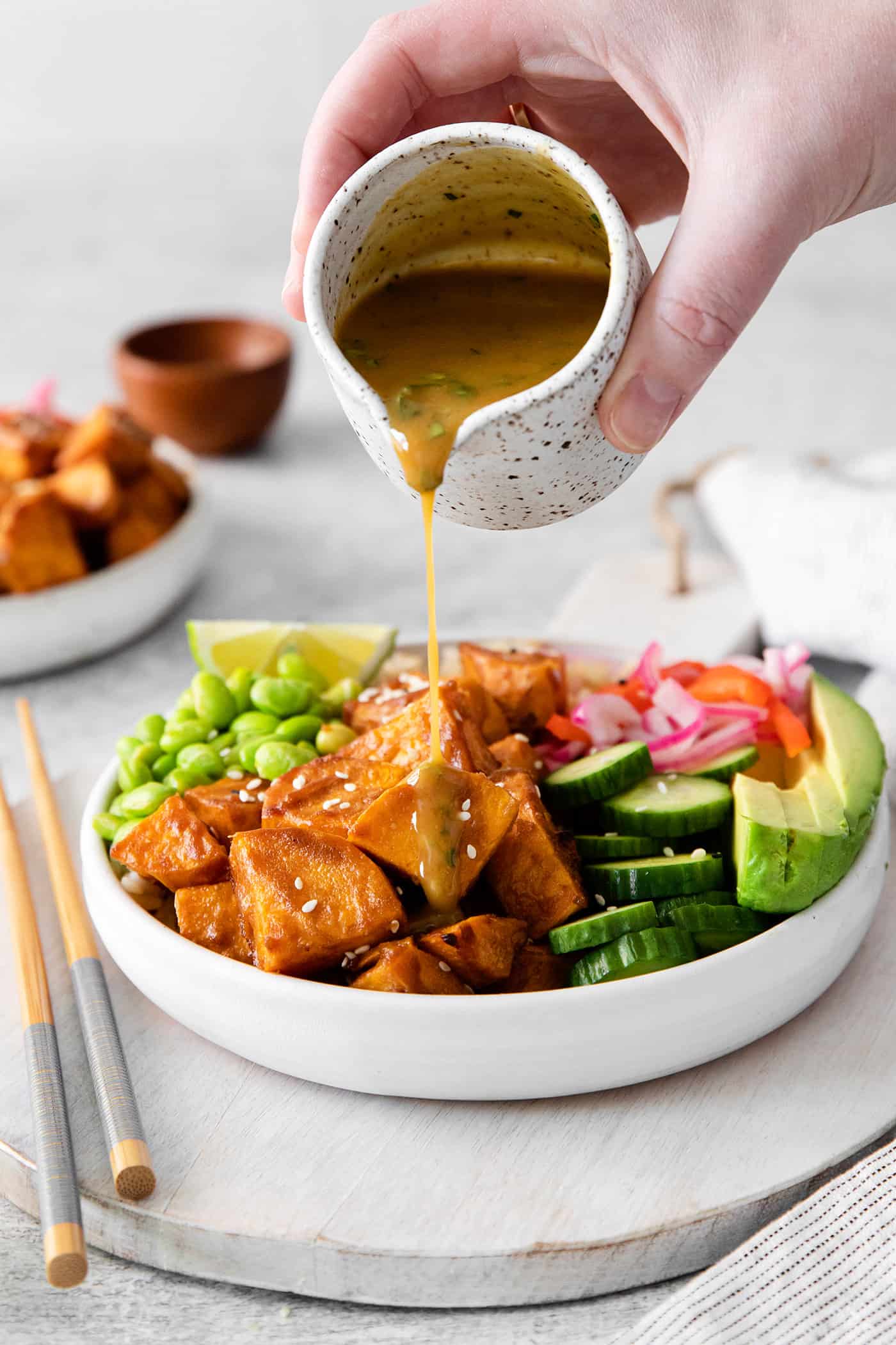 A hand drizzling peanut lime dressing over a vegetarian poke bowl