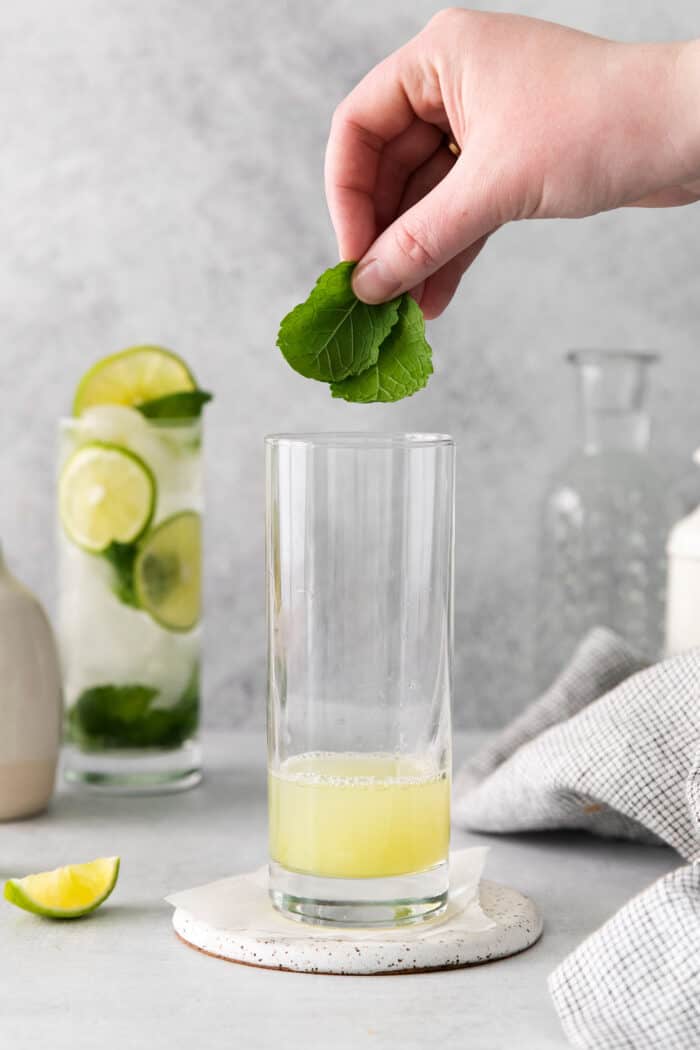 Mint leaves being added to a glass with lime juice