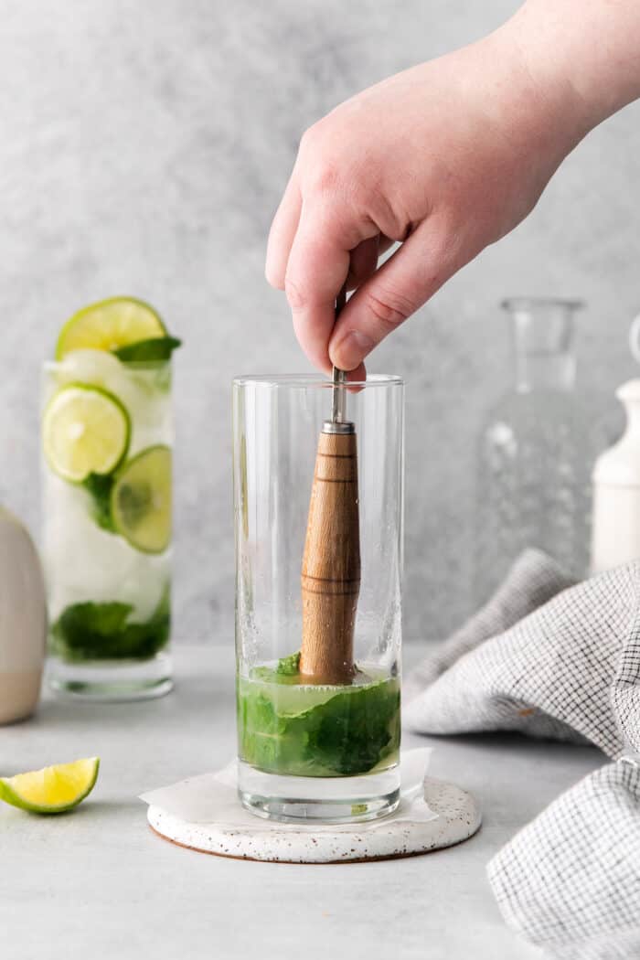 Muddling mint and lime juice in a tall glass