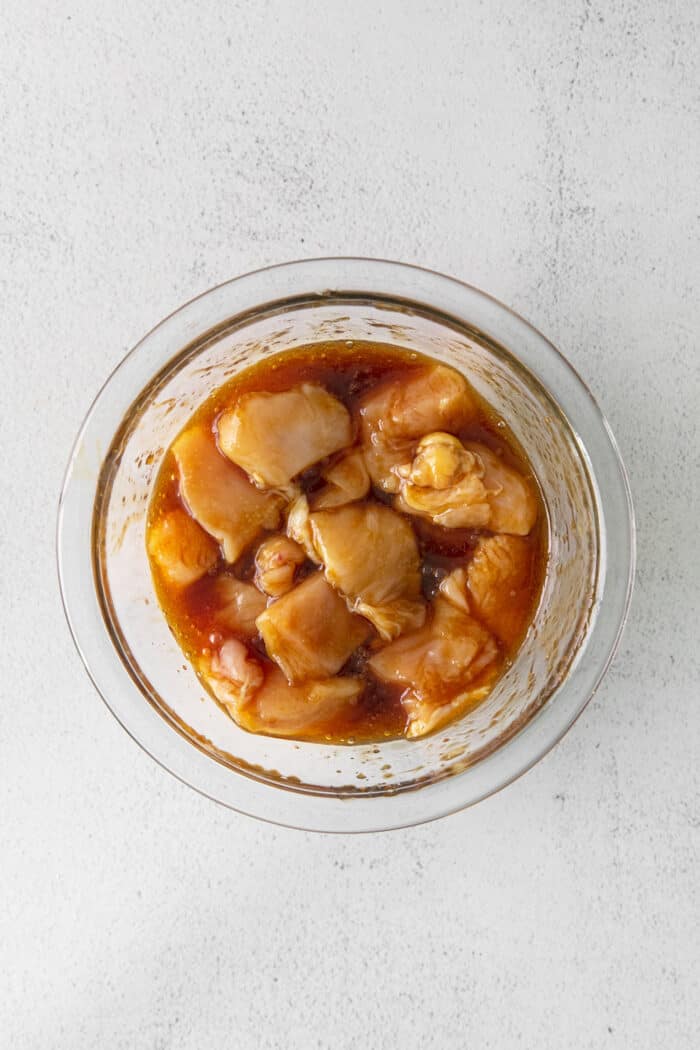Chunks of chicken breast in teriyaki sauce in a mixing bowl