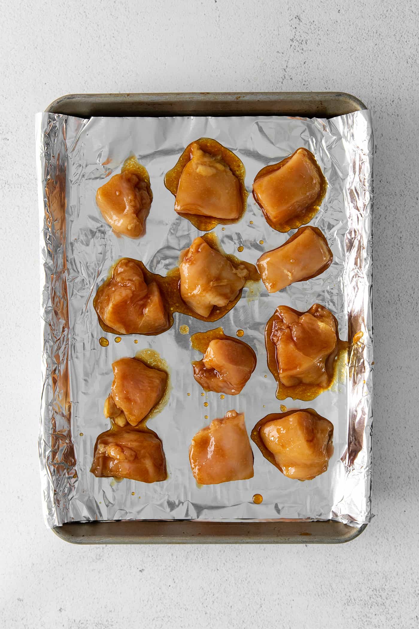 Chunks of teriyaki chicken on foil on a baking sheet