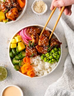 Chopsticks selecting a piece of chicken from a teriyaki chicken poke bowl