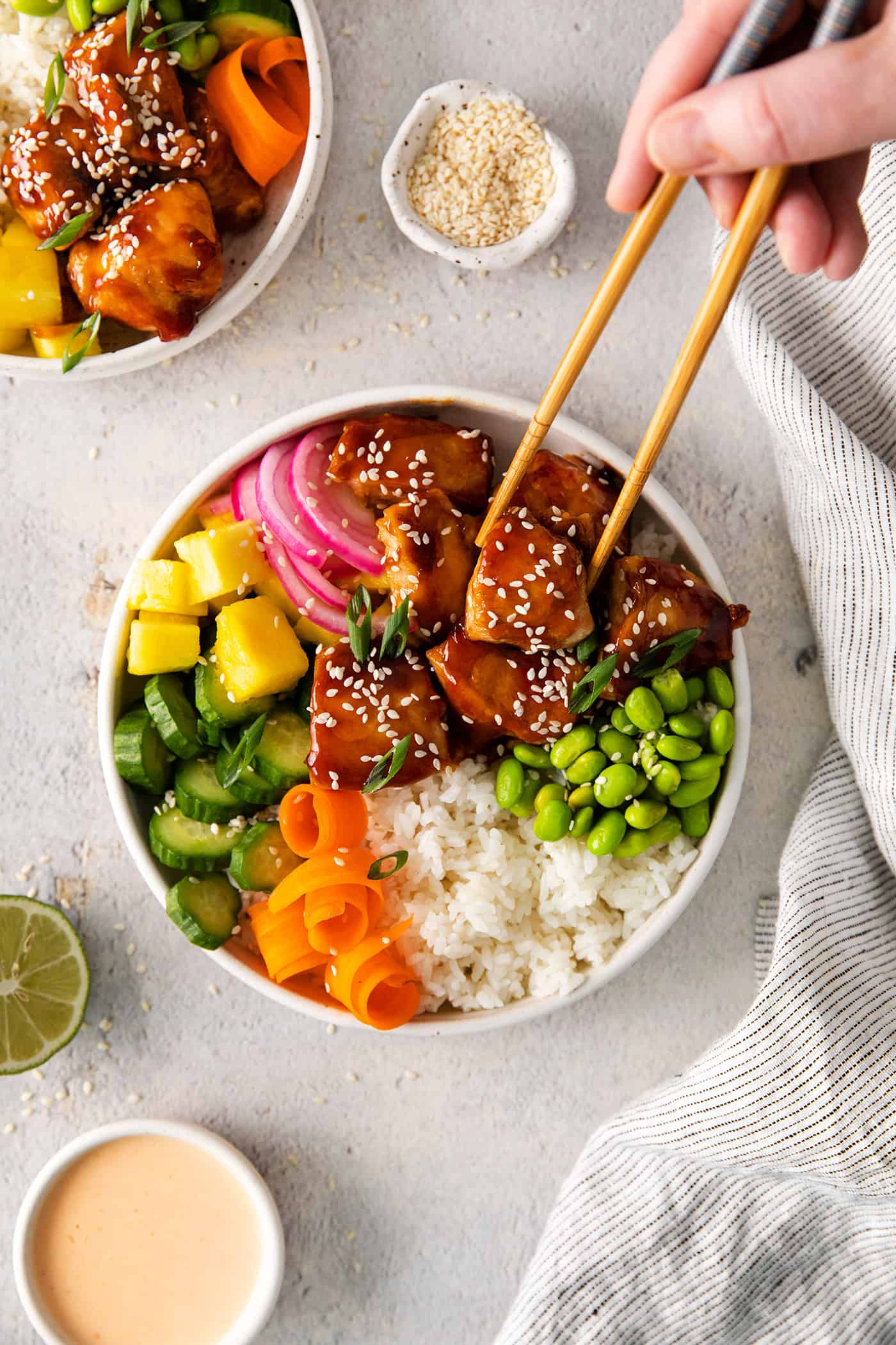 Chopsticks selecting a piece of chicken from a teriyaki chicken poke bowl