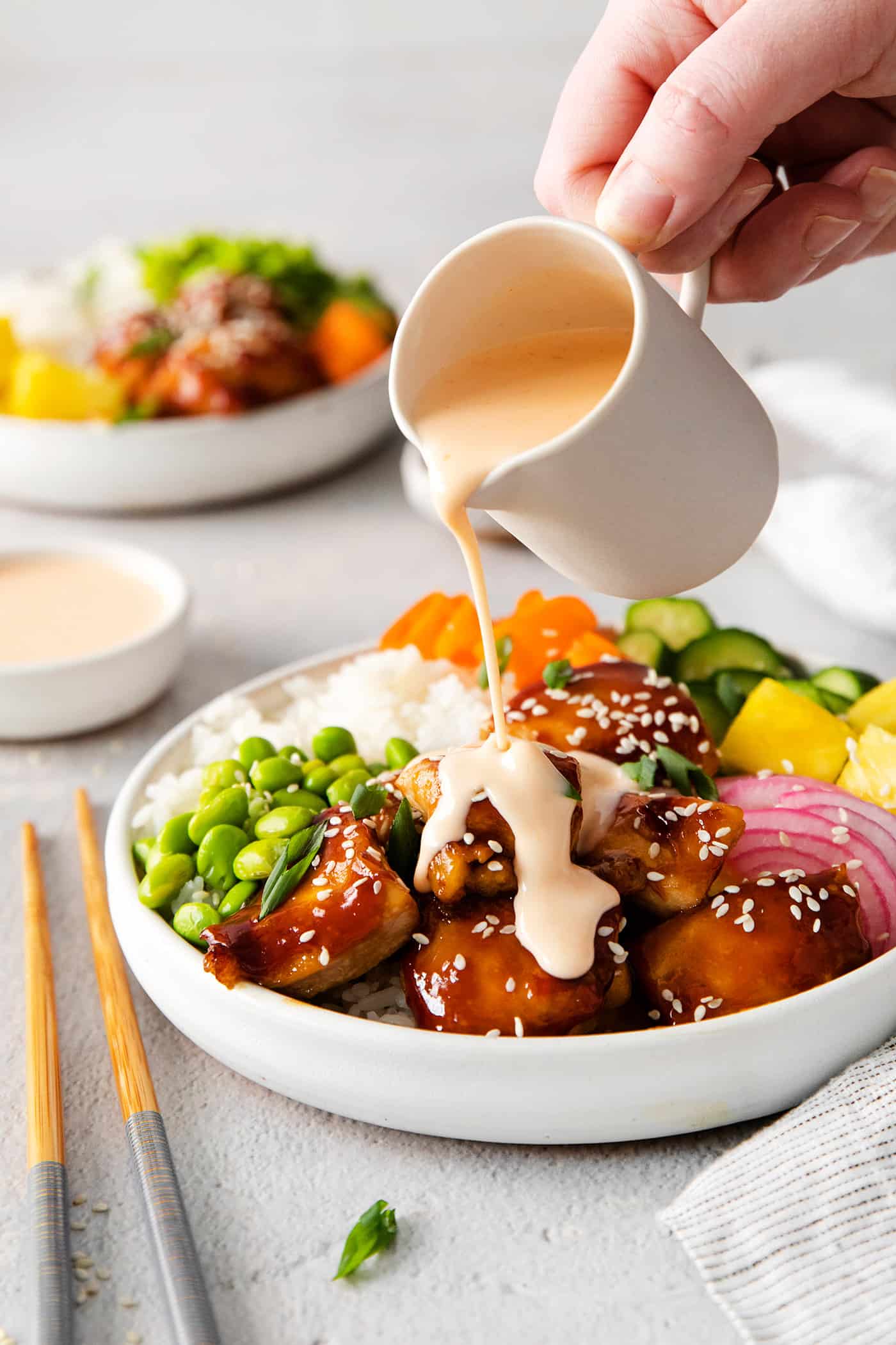 Spicy mayo vinaigrette being poured over a teriyaki chicken poke bowl