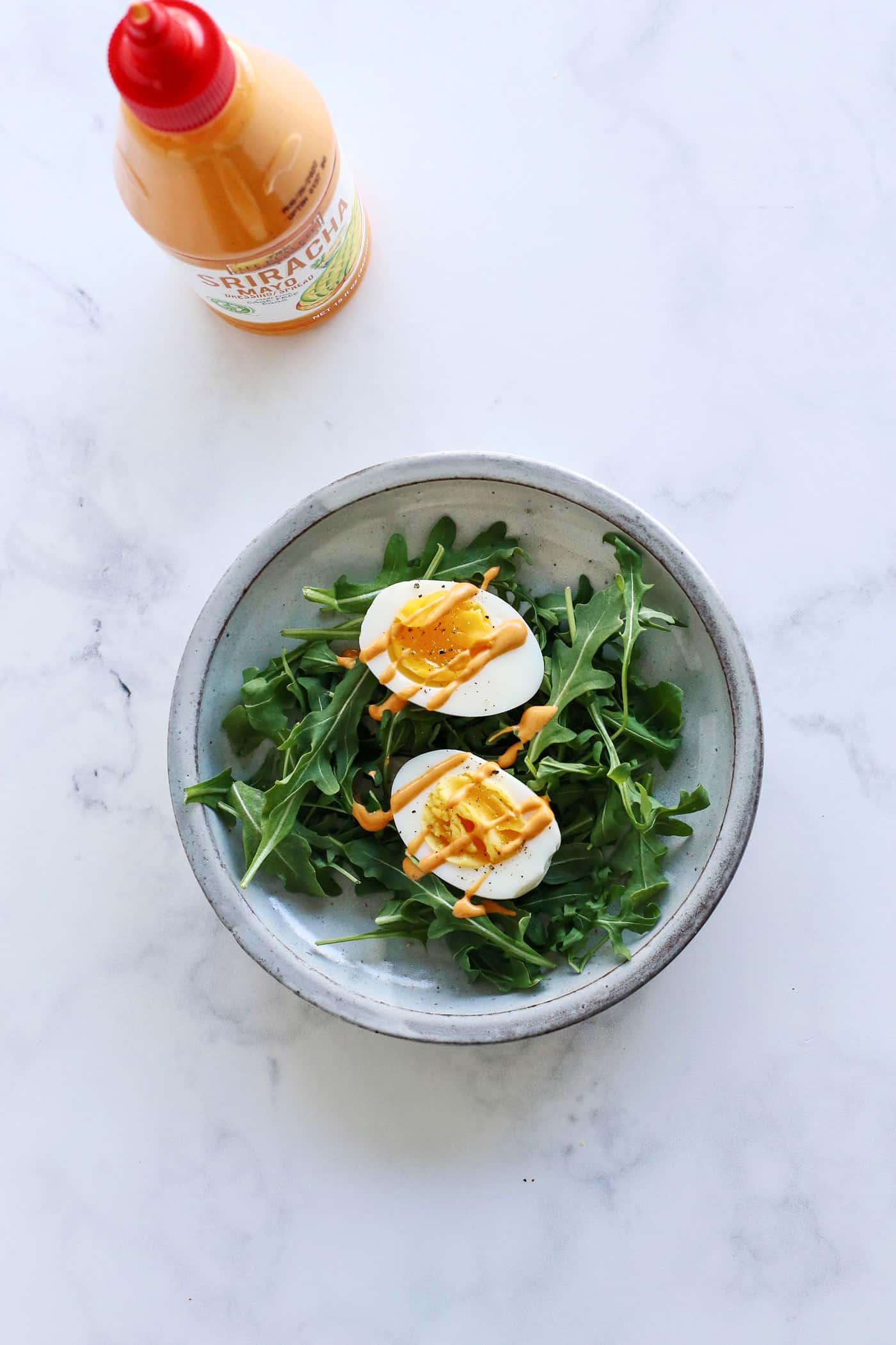 Hard boiled eggs topped with sriracha on arugula