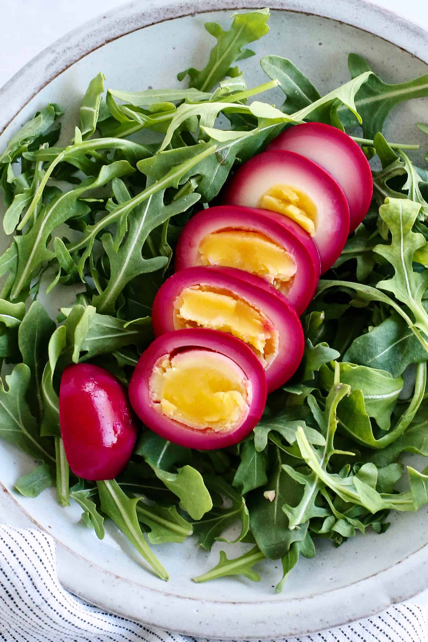 Sliced of beet pickled eggs on a bed of greens