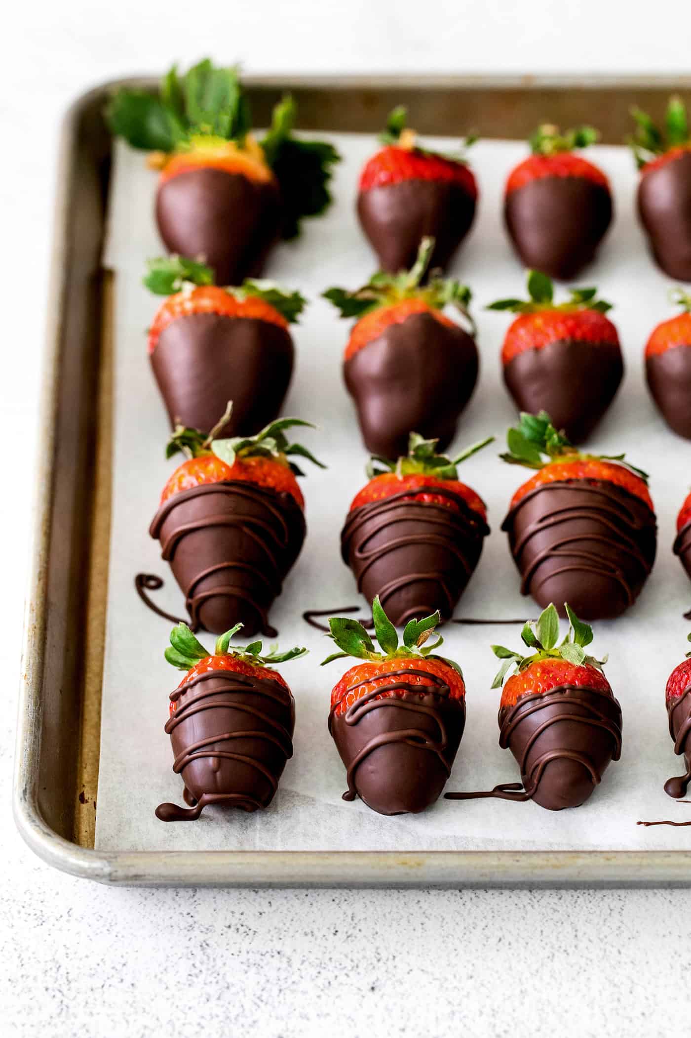 These Chocolate Covered Strawberries may look fancy and elegant, but are actually a quick and easy treat to make, with just 3 ingredients! Overhead view of chocolate dipped strawberries on a baking sheet