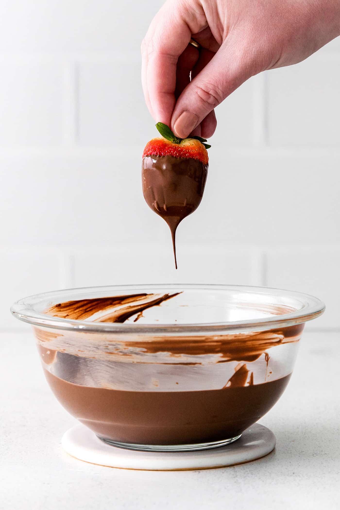 A hand dipping a strawberry into melted chocolate