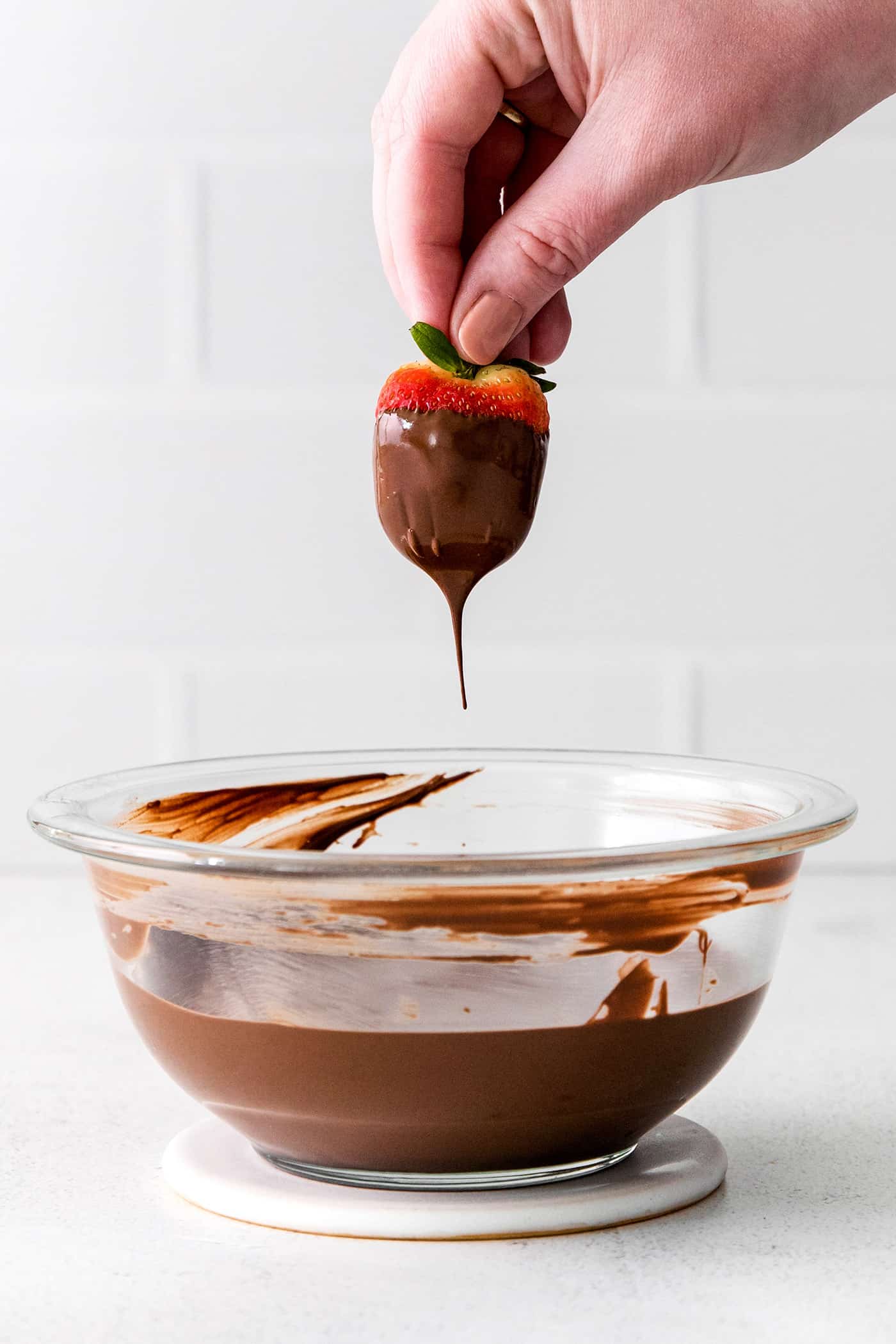 A hand dipping a strawberry into melted chocolate