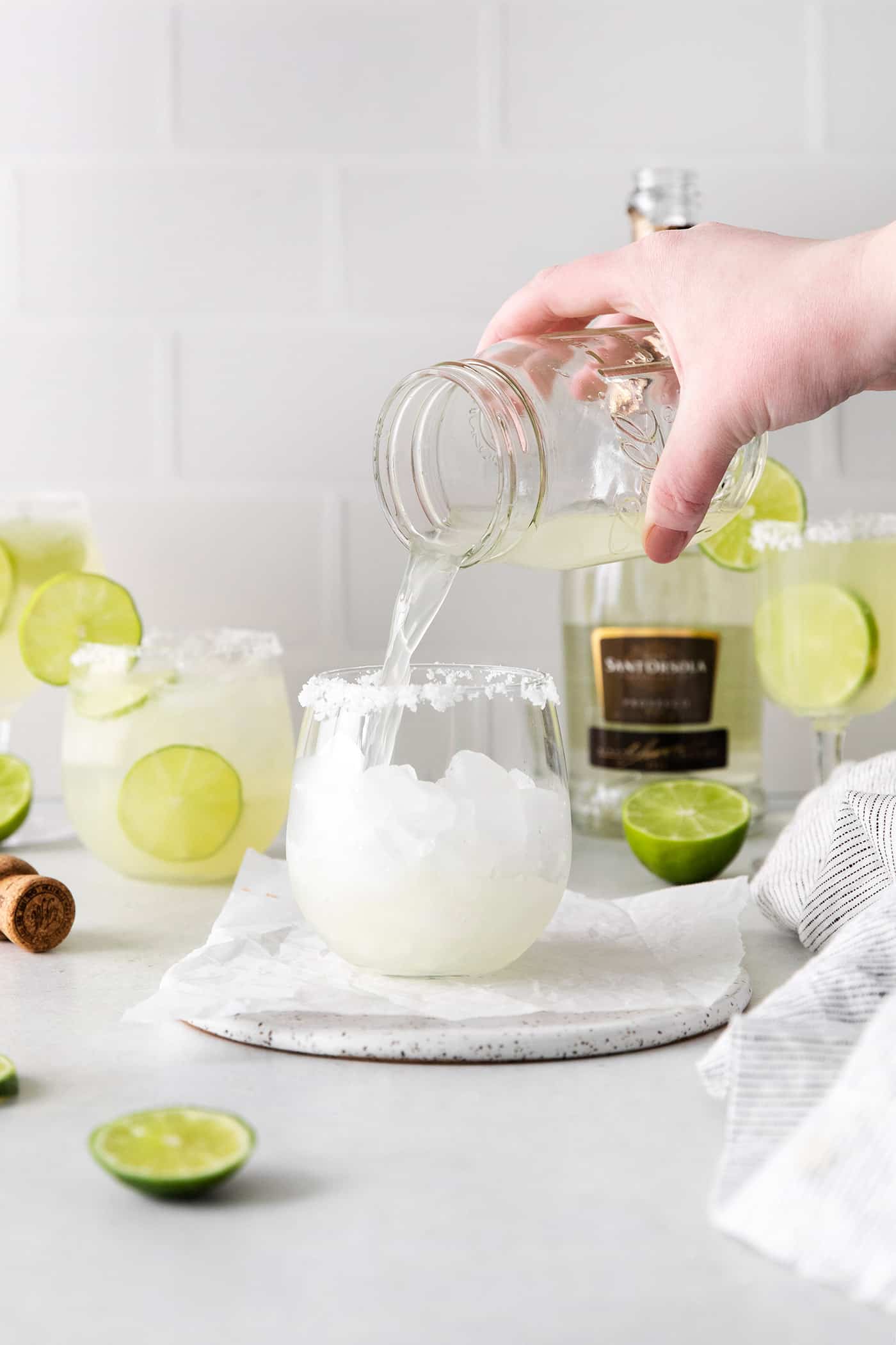 pouring margarita mixture into a drinking glass filled with ice