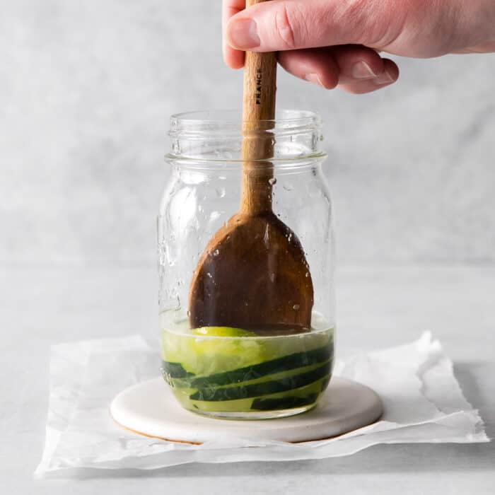 muddling margarita ingredients in a jar with a wooden spoon