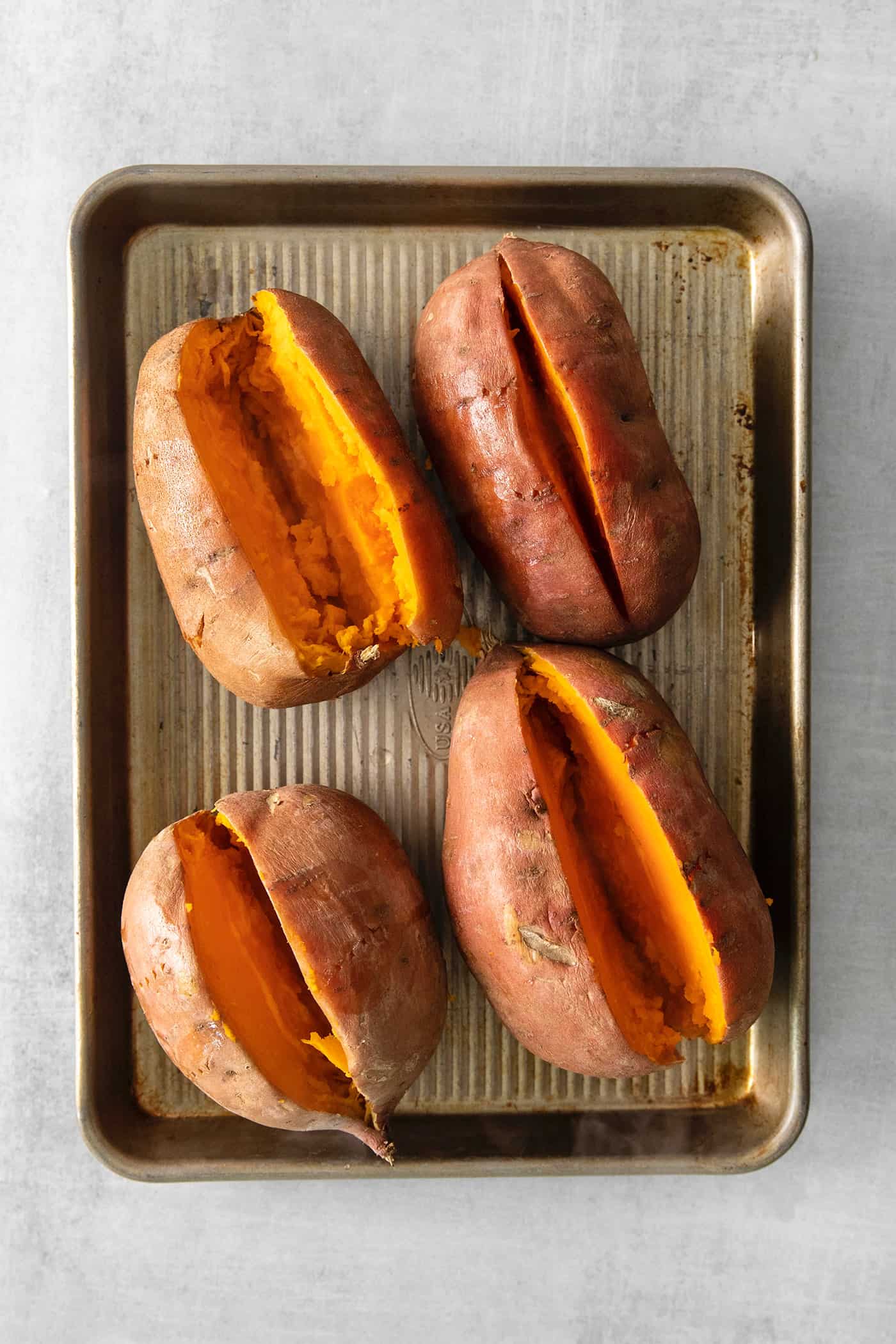 Four cooked sweet potatoes cut open on a baking sheet
