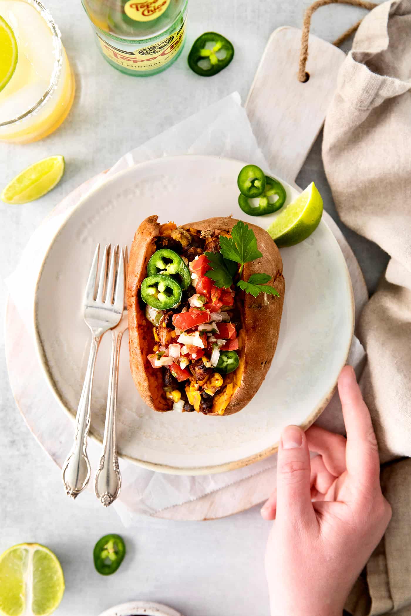 A hand holding a white plate with a stuffed sweet potato