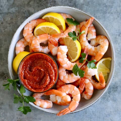 Overhead view of a bowl of shrimp with a dish of cocktail sauce