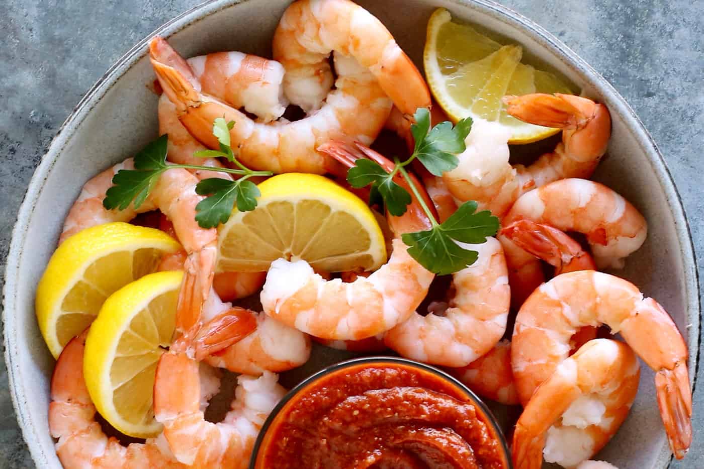 Overhead view of a bowl of shrimp with a dish of cocktail sauce