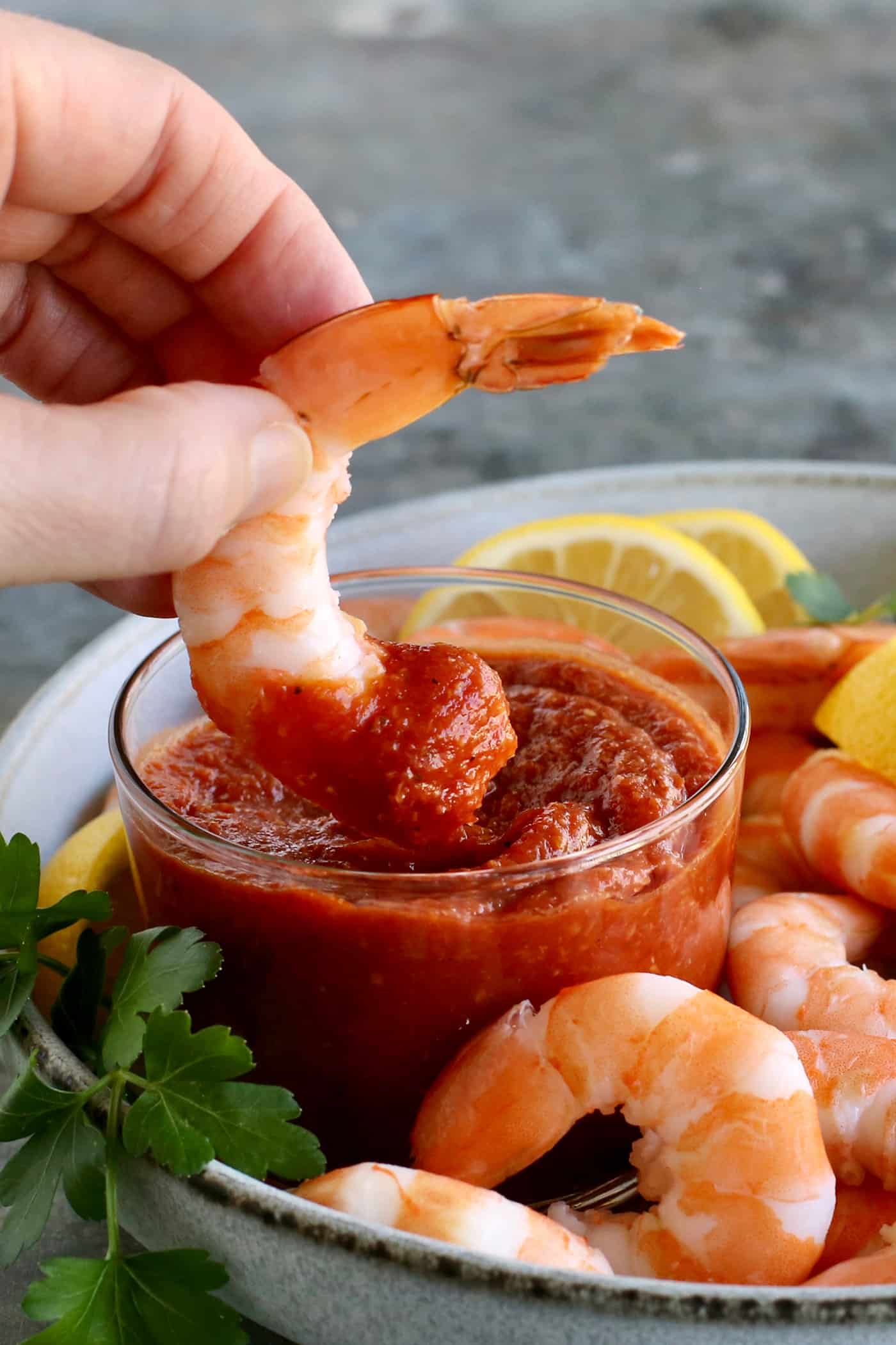 A hand dipping shrimp into a dish of cocktail sauce