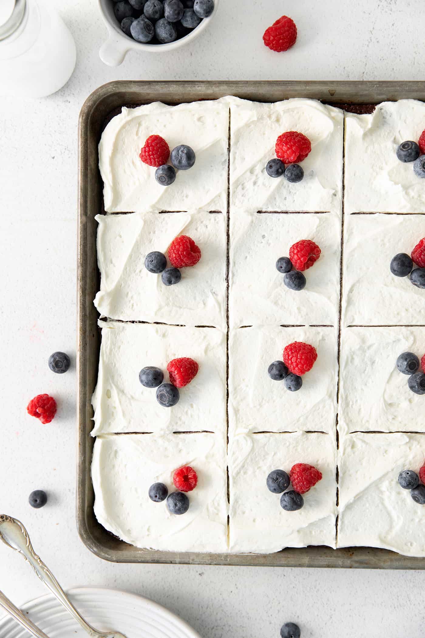 Blueberries and a raspberry on top of each slice of a sliced sheet cake