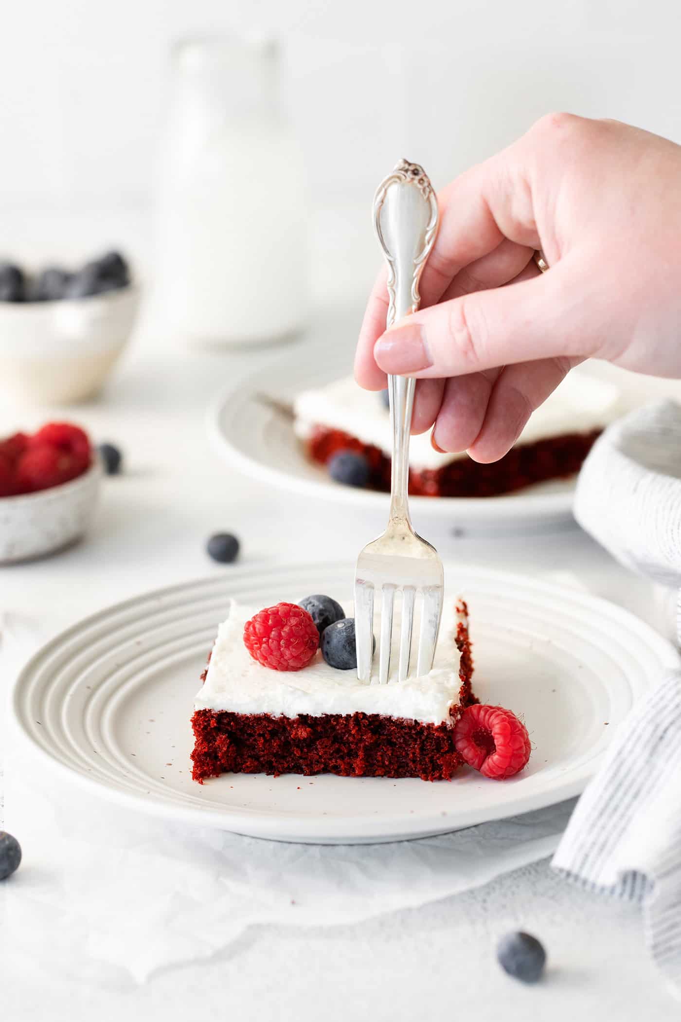 A fork cutting a bite of red velvet cake from a slice on a white plate