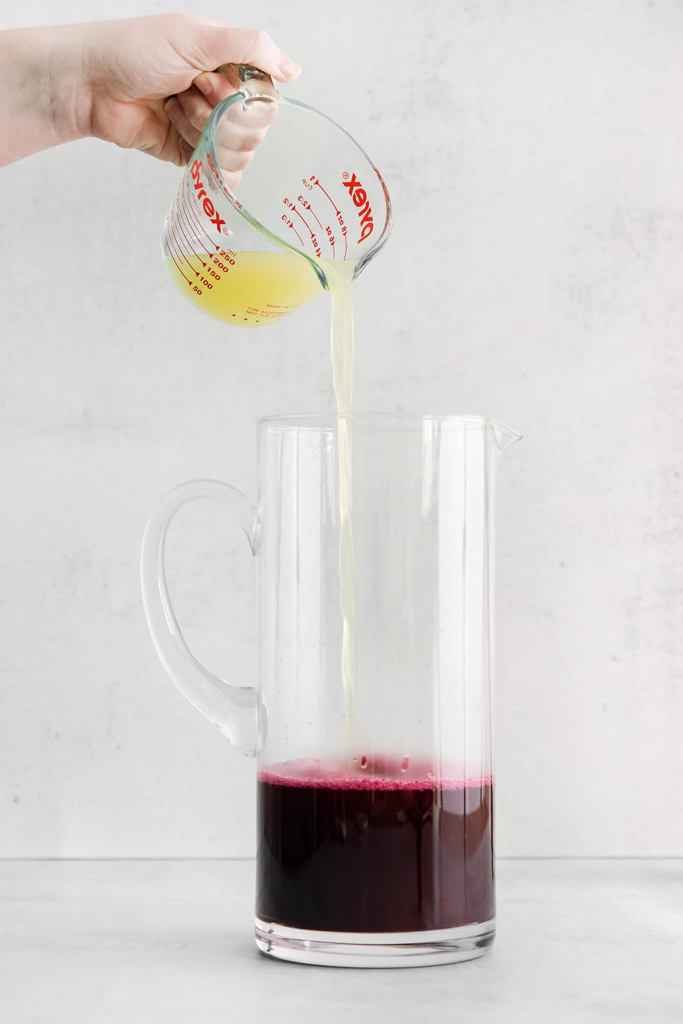 Lemon juice being added to a pitcher with blueberry syrup