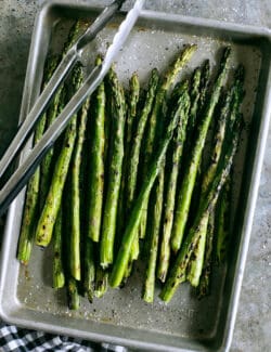 Overhead view of asparagus in a sheet pan with tongs