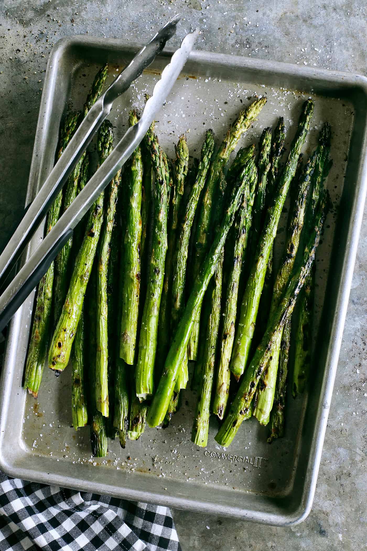 Overhead view of asparagus in a sheet pan with tongs