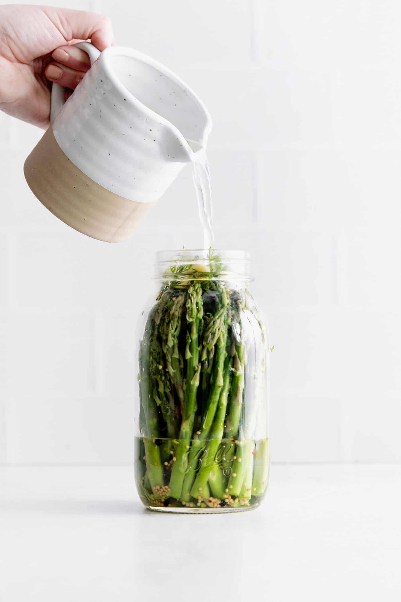 Pickling brine being poured over a jar of asparagus