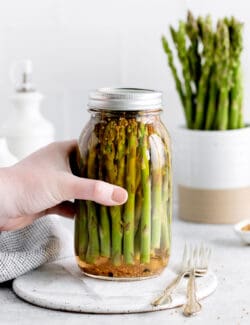 A hand grabbing a jar of asparagus