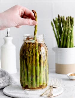 A hand pulling an asparagus from a jar
