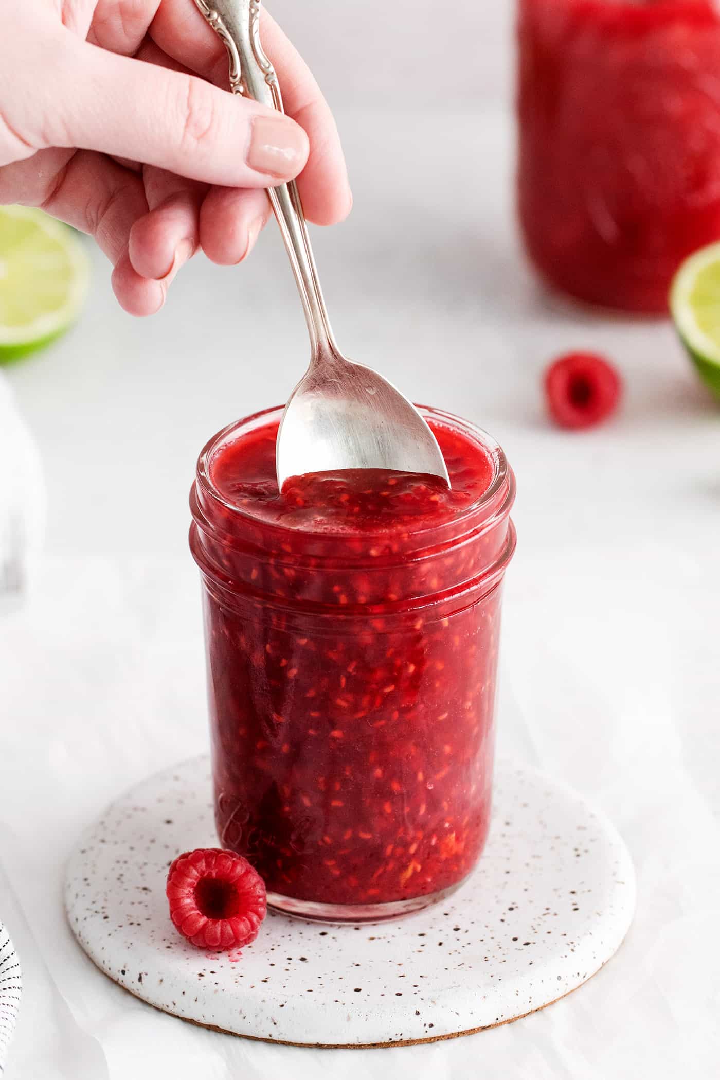 A spoon diving into a jar of raspberry sauce