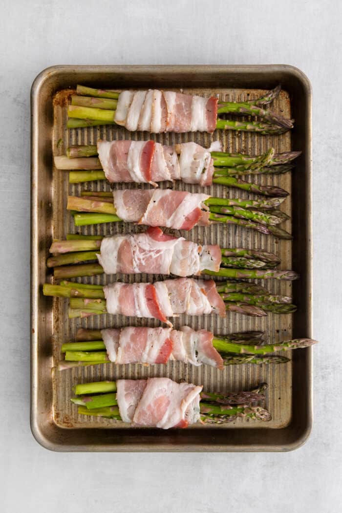 Bundles of asparagus wrapped in bacon on a baking sheet