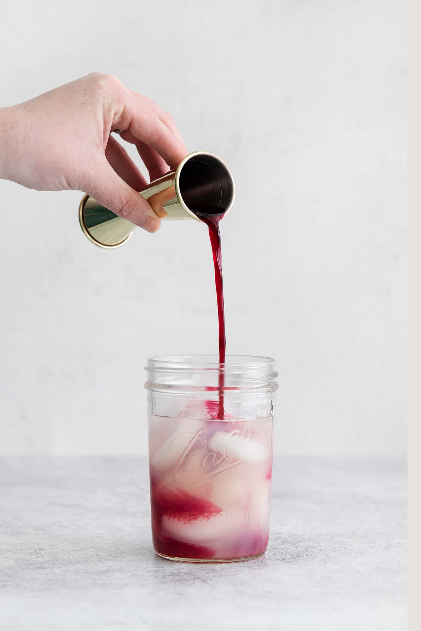 Blueberry simple syrup being poured into a mason jar with ice and tequila